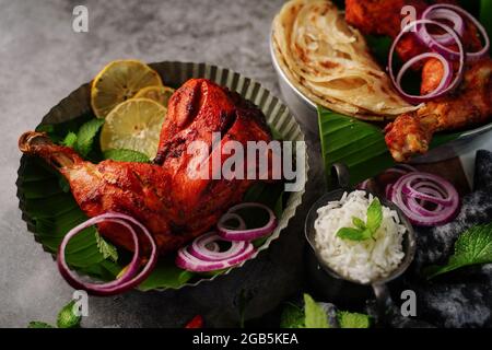 Hausgemachte Tandoori-Hähnchenschenkelstücke, serviert auf einem Teller mit Roti Paratha und Reis – indisches Speisekonzept Stockfoto