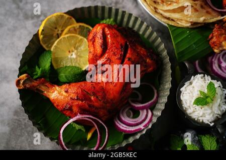 Hausgemachte Tandoori-Hähnchenschenkelstücke, serviert auf einem Teller mit Roti Paratha und Reis – indisches Speisekonzept Stockfoto