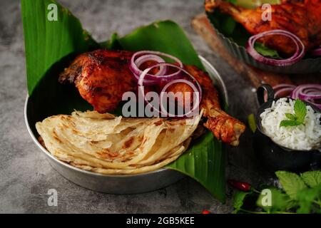 Hausgemachte Tandoori-Hähnchenschenkelstücke, serviert auf einem Teller mit Roti Paratha und Reis – indisches Speisekonzept Stockfoto