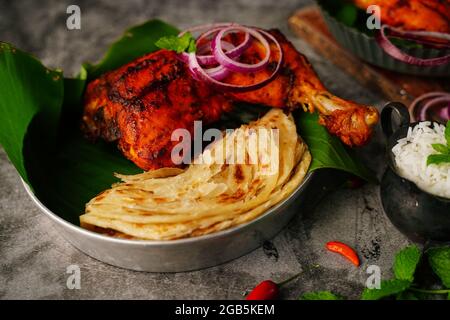 Hausgemachte Tandoori-Hähnchenschenkelstücke, serviert auf einem Teller mit Roti Paratha und Reis – indisches Speisekonzept Stockfoto