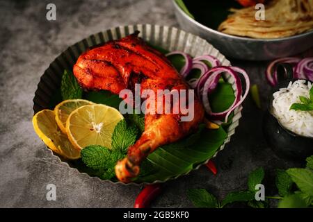 Hausgemachte Tandoori-Hähnchenschenkelstücke, serviert auf einem Teller mit Roti Paratha und Reis – indisches Speisekonzept Stockfoto