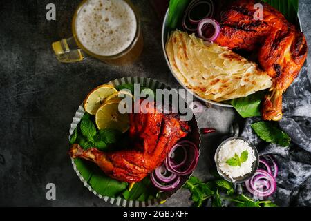 Hausgemachte Tandoori-Hähnchenschenkelstücke, serviert auf einem Teller mit Roti Paratha und Reis – indisches Speisekonzept Stockfoto