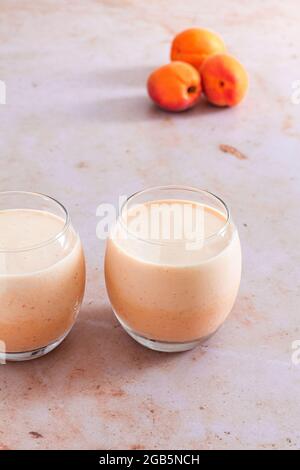 Hausgemachter Aprikosen- und Joghurt-Smoothie in zwei Gläsern mit frischen Aprikosen im Hintergrund. Stockfoto