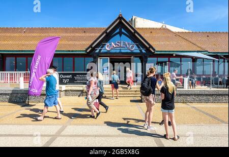 Touristen bummeln in der Familie oder zwischen Freunden entlang der Strandpromenade in Etretat, Frankreich, und gehen an einem sonnigen Tag am Eingang des Casinos vorbei. Stockfoto