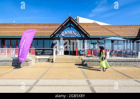 Ein paar Touristen schlendern entlang der Küste in Etretat, Frankreich, und gehen an einem sonnigen Tag zum Casino-Eingang. Stockfoto