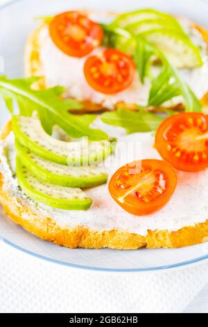 Zwei Toasts mit Avocado und Rucola auf einem Teller. Avocado-Toasts mit Frischkäse und Kirschtomaten. Diät-Essen. Nahaufnahme Stockfoto