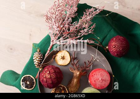 Weihnachtliche Komposition in Burgunder- und Brauntönen, weihnachtsbaumschmuck und Kerzen, Trockenfrüchte und Deko-Hirsche auf einer grünen Tischdecke Stockfoto