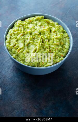 Guacamole in einer grauen Schale auf dunklem Grund. Schüssel mit Avocado-Guacamole-Sauce mit frischen Zutaten. Speicherplatz kopieren. Draufsicht Stockfoto