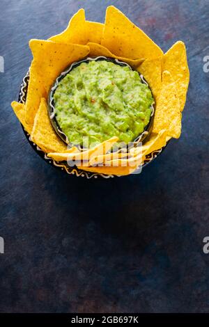 Traditionelle mexikanische Sauce Guacamole mit Tortilla-Chips in Tonschüssel. Schüssel mit Guacamole mit Nachos-Chips auf dunklem Hintergrund. Speicherplatz kopieren. Draufsicht Stockfoto