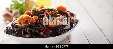 Herzhafte schwarze Spaghetti mit Garnelen, die zum Mittagessen in einer Schüssel auf dem Holztisch im Restaurant serviert werden Stockfoto