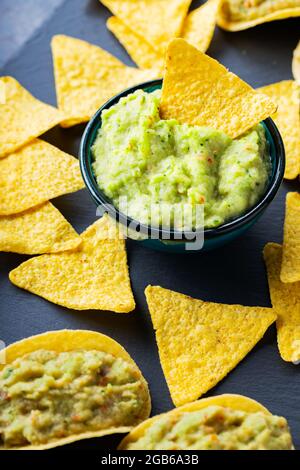 Guacamole- und Nachos-Chips auf dunklem Hintergrund. Guacamole-Sauce mit Mais-Chips auf einem Schieferbrett. Nahaufnahme. Selektiver Fokus Stockfoto