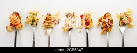 Draufsicht auf Gabeln und Löffel mit verschiedenen Arten von leckeren Pasta in Reihe auf grauem Hintergrund platziert Stockfoto