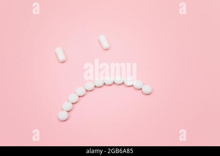 Pharma-Schaden. Trauriges Smiley-Gesicht aus White Pills, auf Pink Backgrond liegend. Globale Pharmaindustrie und Arzneimittel Stockfoto