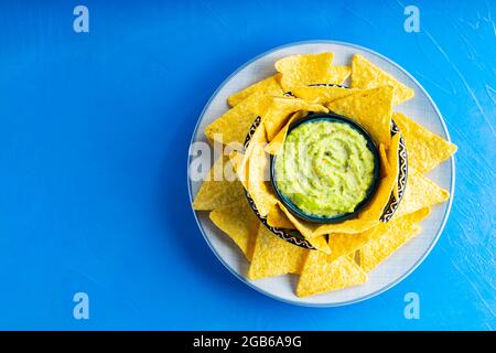 Tortilla-Chips und Guacamole-Sauce auf blauem Hintergrund. Guacamole mit Maissplittern auf einem Teller. Speicherplatz kopieren. Draufsicht Stockfoto