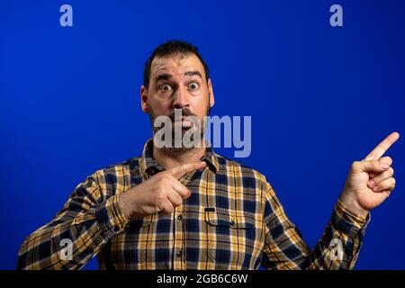 Seitenaufnahme eines jungen Mannes, der mit einem Finger auf blauem Hintergrund stand und mit jemandem diskutierte. Stockfoto
