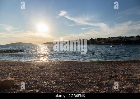 Schöner Sommeruntergang über der kleinen Stadt Rogoznica, mit offenem Adriatischen Meer, das die felsige Küste bespritzt Stockfoto