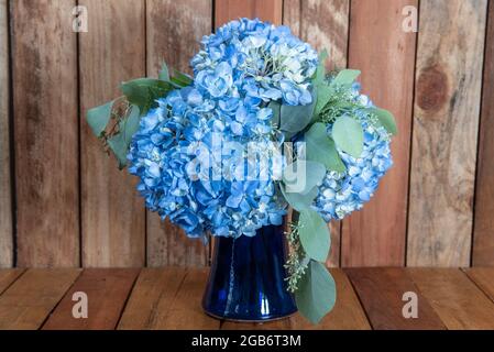 Schöner Strauß von arrangierten blauen Hydrongea Blumen in einer blauen Vase, die als emotionales Gefühl gegeben wird. Stockfoto