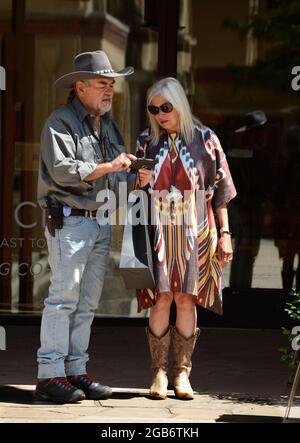 Ein Paar, das in westlicher Kleidung gekleidet ist, benutzt sein Smartphone, als sie Santa Fe, New Mexico, besuchen. Stockfoto
