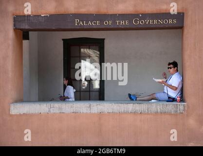 Eine Frau isst zu Mittag, während sie sich an einer Wand des historischen Gouverneurspalasts aus dem 17. Jahrhundert in Santa Fe, New Mexico, entspannt. Stockfoto