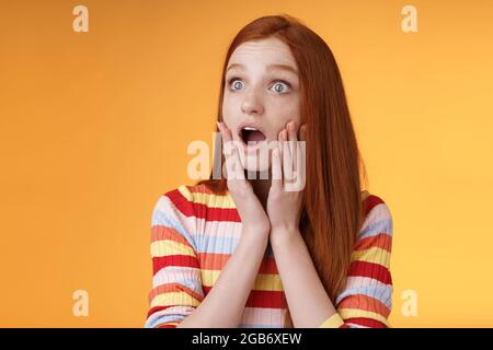 Schockiert erstaunt junge Drama Mädchen rothaarige blaue Augen keuchend Empathie Berühren Wangen schockiert Tropfen Kiefer Sorge drehen links überrascht Stehend Stockfoto