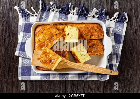 kartoffelkugel, gebackener Pudding oder Auflauf geriebener Kartoffeln, die in Portionen in einer Auflaufform auf einem Holztisch geschnitten werden, jüdisches Feiertagsrezept Stockfoto