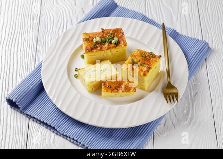 Herzhafte Kartoffel-kugel, gebackener Pudding oder Auflauf geriebener Kartoffeln auf einem weißen Teller auf einem weißen Holztisch, jüdisches Feiertagsrezept Stockfoto