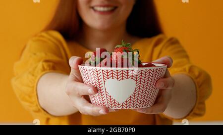 Nahaufnahme eines fröhlichen charmanten Kaukasus, der eine köstliche Erdbeere auf gelbem Hintergrund verkostet. Gesunde Ernährung Stockfoto