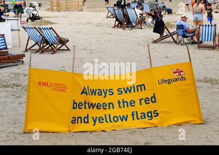 Weymouth, England - 2021. Juli: RNLI-Schild, auf dem Besucher aus Sicherheitsgründen zwischen den roten und gelben Flaggen schwimmen sollten. Stockfoto