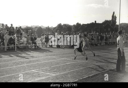 1964, historisch, beobachtet von Zuschauern, zwei Teenager, die am Schulsporttag auf einer Schlapprennbahn im Sprint-Rennen gegeneinander antreten, wobei einer der Jungen das Rennen gewann, als er das Ziellaufband zuerst erreicht hat, Exeter, England, Großbritannien. Stockfoto