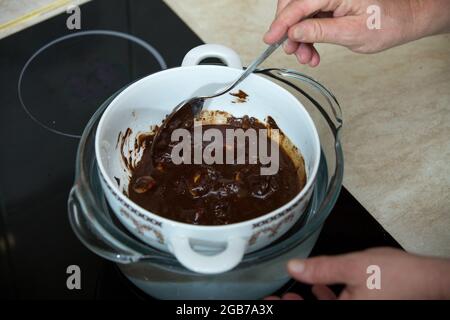 Schritt-für-Schritt-Prozess der Herstellung von Schokolade aus dunkler Schokolade und Kirschen in Cognac zu Hause. Der Prozess, bei dem die Zutaten für Schokolade geschmolzen werden Stockfoto