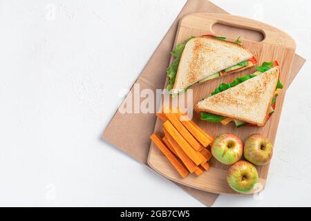 Vorbereitung eines Schulfrühstücks. Sandwich, Karotten und Äpfel auf einem Schneidebrett auf grauem Hintergrund. Draufsicht, Panorama. Stockfoto