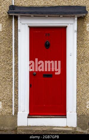 Die Hausnummer 32 auf einem rot bemalten Türrahmen aus Holz in Hertfordshire, mit einem Messingklopfer und einem Briefkasten mit Griff. Stockfoto