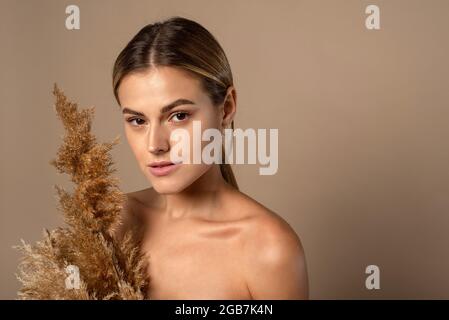 Eine schöne junge Frau mit zurückgezogenem Haar hält ein trockenes Pampagras in ihren Händen. Das Konzept der Naturkosmetik aus Weizenkörnern. Hautpflege Stockfoto