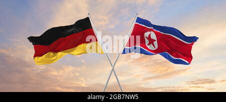 Flaggen von Deutschland und Nordkorea winken im Wind auf Fahnenmasten gegen den Himmel mit Wolken am sonnigen Tag. Symbolisieren Beziehung, Dialog zwischen zwei c Stockfoto
