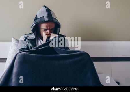 Junger Mann mit Depressionen auf dem Bett sitzend. Stockfoto