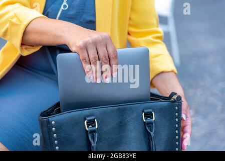 Nicht erkennbare weiße Geschäftsfrau, die ihren Laptop in ihrer Handtasche speichert Stockfoto