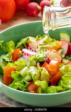 Frischer Gemüsesalat mit Olivenöl in Keramikschale auf Holzgrund. Sommergericht mit Tomaten, Gurken und Radieschen. Stockfoto