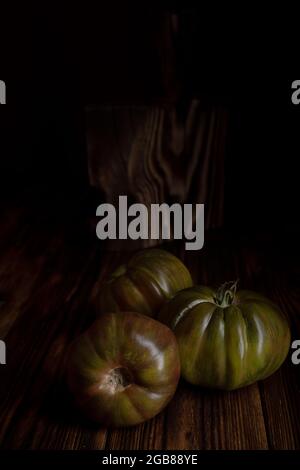 Rote gerippte Tomaten auf einem schönen Holzschneidebrett auf einem Holzhintergrund. Low-Key-Foto Stockfoto