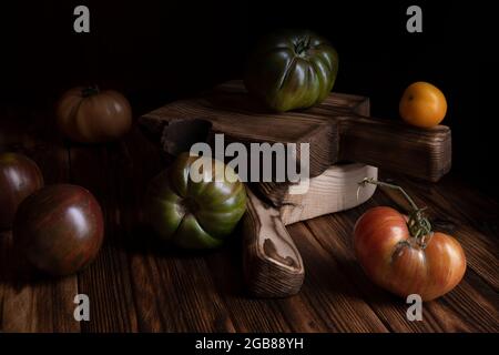 Rote gerippte Tomaten auf einem schönen Holzschneidebrett auf einem Holzhintergrund. Low-Key-Foto Stockfoto