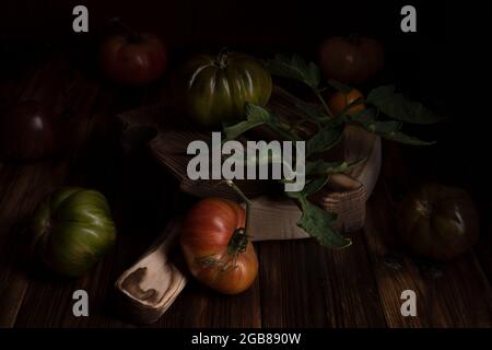 Rote gerippte Tomaten auf einem schönen Holzschneidebrett auf einem Holzhintergrund. Low-Key-Foto Stockfoto