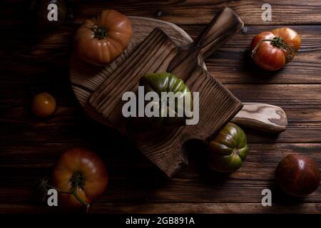 Rote gerippte Tomaten auf einem schönen Holzschneidebrett auf einem Holzhintergrund. Low-Key-Foto Stockfoto