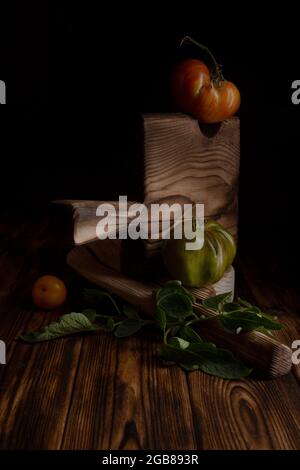 Rote gerippte Tomaten auf einem schönen Holzschneidebrett auf einem Holzhintergrund. Low-Key-Foto Stockfoto