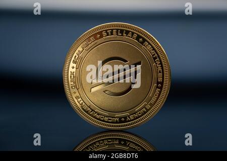 Stellar XLM Lumen Cryptocurrency Physical Coin placed on the reflective blue surface Stockfoto