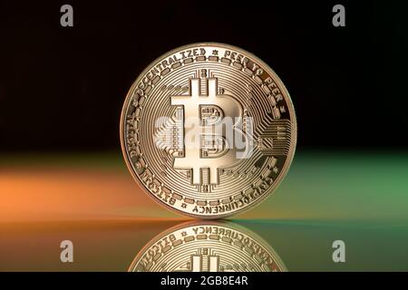 Bitcoin BTC Kryptowährung physische Münze auf reflektierender Oberfläche platziert und mit grünen und roten Lichtern beleuchtet Stockfoto