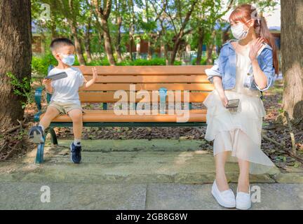 Mutter und Sohn in sozialer Distanzierung sitzen auf der Bank im Park Stockfoto