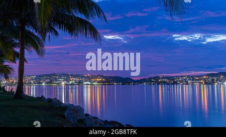 Der Strand und die Bucht im Sommer mit dem Himmel spiegelt sich in einem ruhigen Wasser umgeben von Felsen und Palmen in der goldenen und blauen Stunde Stockfoto
