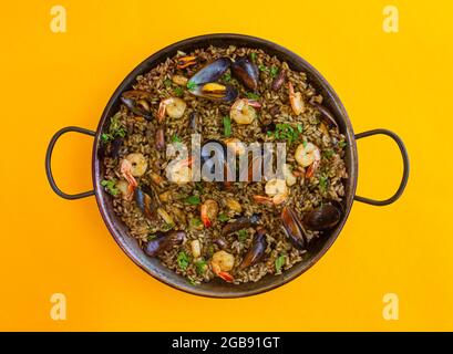 Schwarze Paella mit Reis, Garnelen, Muscheln und Tintenfisch auf gelbem Hintergrund Stockfoto