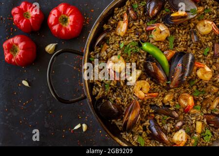 Schwarze Paella mit Meeresfrüchten und Tintenfisch mit Tomaten auf schwarzem Hintergrund Stockfoto