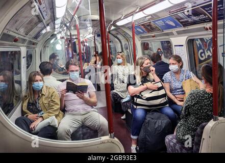 London, Großbritannien. Juli 2021. Passagiere mit Gesichtsmasken plaudern und lesen ein Buch in einem Zug der Bakerloo Line. Trotz des Endes der gesetzlichen Pflicht zum Tragen von Gesichtsmasken in England ist das Tragen von Gesichtsmasken auf Londoner Transportmitteln weiterhin obligatorisch und die Menschen halten sich weiterhin an die Vorschriften. (Foto von Martin Pope/SOPA Images/Sipa USA) Quelle: SIPA USA/Alamy Live News Stockfoto