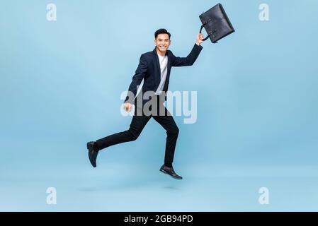 Porträt eines lächelnden jungen, gutaussehenden asiatischen Büroarbeiters, der in einer mittleren Tragetasche in hellblauem, isoliertem Studiohintergrund läuft Stockfoto